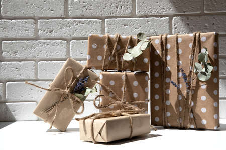 A set of handmade gifts in kraft paper, tied with wide twine, decorated with dry flowers on a white...