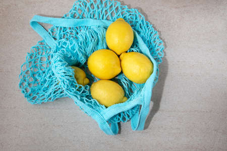 Blue mesh eco bag with fresh lemons and limes on a light stone background. Top viewの写真素材