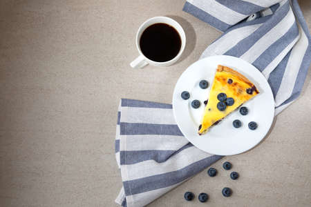 A piece of blueberry cheesecake on a white plate and a cup of coffee on a stone table. Top viewの写真素材