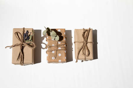 A set of handmade gifts in kraft paper, tied with wide twine, decorated with dry flowers on a white table. Top viewの写真素材