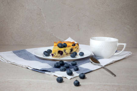 A piece of blueberry cheesecake on a white plate and a cup of coffee on a stone table. Front viewの写真素材