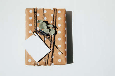 The gift is wrapped in kraft paper with white circles, tied with twine, decorated with dry flowers...