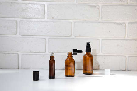 Tree open amber bottles with natural cosmetics on a white table and brick wall. Front viewの写真素材