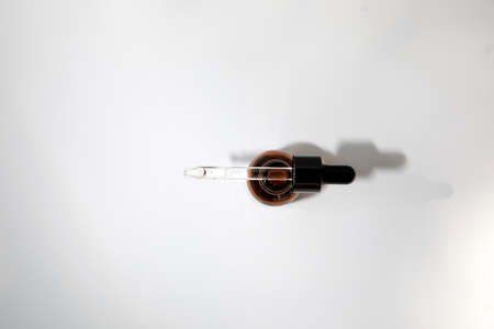 One open amber bottle with a pipette on a white table, selfcare cosmetic products. Top viewの写真素材