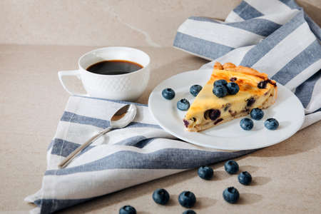A piece of blueberry cheesecake on a white plate and a cup of coffee on a stone table. Front viewの写真素材