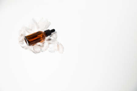 An amber bottle with pipettte on a white feather on a white table with face serum product. Glass bottle with self care product. Top viewの写真素材