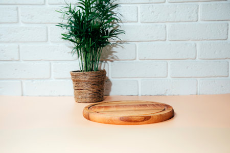 Wooden round board, pedestal, on white table with indoor palm tree with free space for inscription. Front viewの写真素材