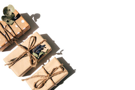 A set of handmade gifts in kraft paper, tied with wide twine, decorated with dry flowers on a white table. Top viewの写真素材