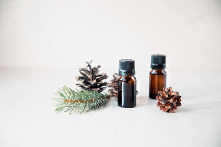Aroma oil in amber bottles on a light stone background with a coniferous branch and dry pine cones. Front viewの写真素材