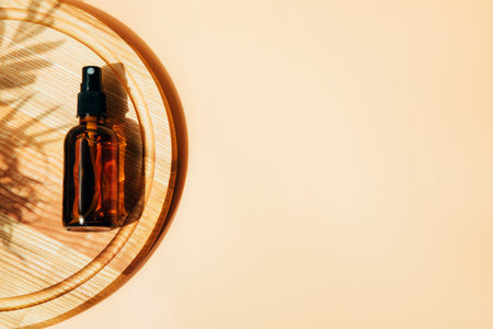 One amber bottle on wooden board with face care products. Spray in a glass package. Top view with palm leaf shadowの写真素材