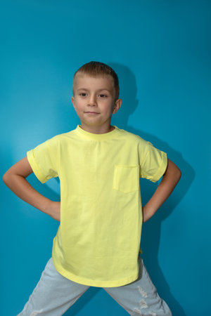 A joyful boy of 6-7 years old in a yellow t-shirt on a blue background close-up shows thumbs up. Front viewの写真素材