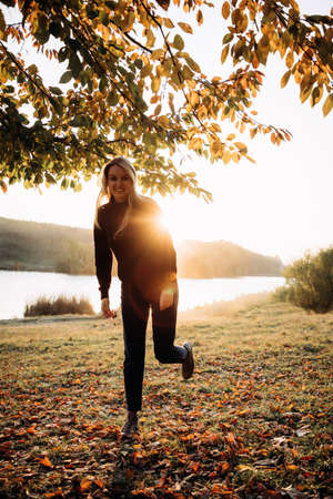Beautiful girl with long blond hair in autumn landscape at sunset. Autumn portrait of a girl with the sun behind her, front viewの写真素材