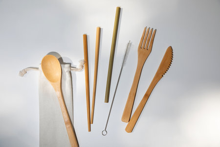 Eco wooden cutlery, spoon, fork, knife and bamboo straws on a textile bag on a white background. Top...