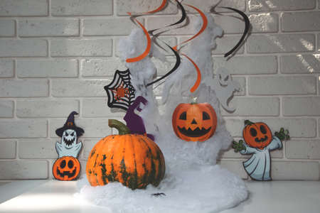 Pumpkin, cobwebs with spiders on a white table against a white brick wall background. Halloween composition with shadows, front view, selective focusの写真素材