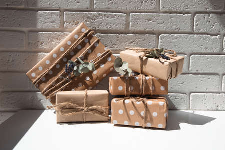A set of handmade gifts in kraft paper, tied with wide twine, decorated with dry flowers on a white table. Front viewの写真素材