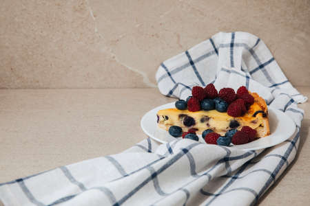 A piece of blueberry cheesecake on a white plate with raspberry on a white towel in a cage. Front viewの写真素材