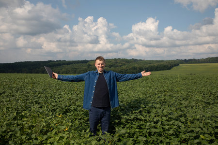 A farmer with a tablet checks the quality of soybeans in an agricultural field and is happy with the harvest. Front viewの写真素材