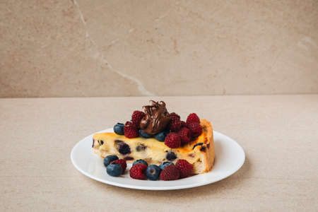 A piece of blueberry cheesecake on a white plate with fresh raspberries and blueberries on a stone table. Front viewの写真素材