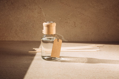 Aroma diffuser in a clear glass bottle with a wooden cap on a light stone background with wooden sticks behind. Front viewの写真素材