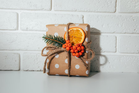 A gift in eco packaging, wrapped in brown paper, decorated with a dry orange and a fir branch. New Years gift on white background, front viewの写真素材