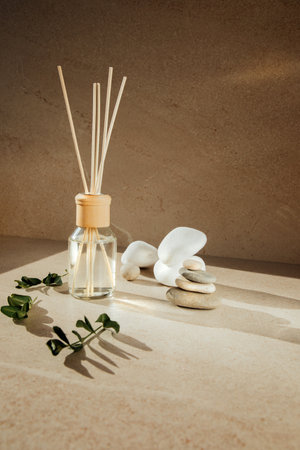 Aroma diffuser in a clear glass bottle with a wooden cap on a light stone background with wooden sticks behind and green branches. Front viewの写真素材