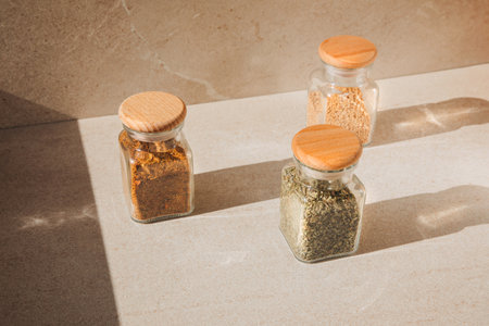 A group of seasoning in glass jars on a light stone background with shadows. Paprika, herbs, mustard, garlic, top view, selective focusの写真素材