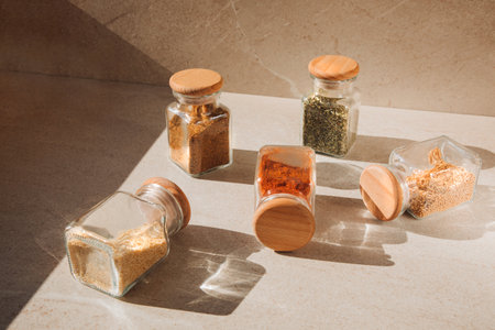 A group of seasoning in glass jars on a light stone background with shadows. Paprika, herbs, mustard, garlic, front view, selective focusの写真素材