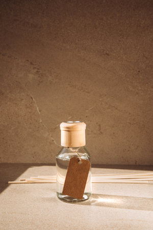 Aroma diffuser in a clear glass bottle with a wooden cap on a light stone background with wooden sticks behind. Front viewの写真素材