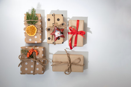 A gifts in eco packaging, wrapped in brown paper, decorated with a dry orange, cinnamon stick, fir branch and red ribbon. Gift on white background, top viewの写真素材