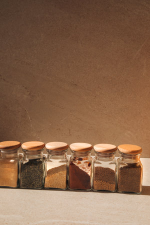 A group of seasonings in glass jars on a light stone background with shadows. Paprika, herbs, mustard, garlic, front view, selective focusの写真素材