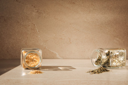 Seasonings in open glass jars on a light stone background with shadows. Dry herbs, mustard, garlic, top view, selective focusの写真素材