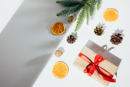 A gift wrapped in brown paper and tied red ribbon with a fir branch, a golden toy and a pine cone, orange on a white background. Top viewの写真素材