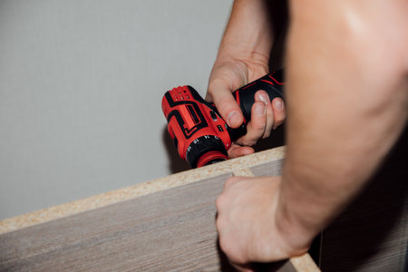 Close-up of male hands with a red screwdriver when assembling a cabinet, furniture. Top viewの写真素材