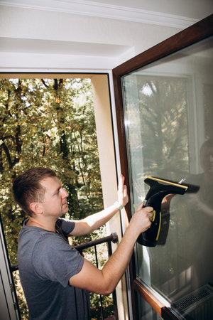 The man washes the windows at home using a cordless window cleaner, cleaning the house. Top view, selective focusの写真素材