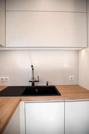 Kitchen interior. A black washbasin, tall brass faucet in a white kitchen with a wooden countertop. Front viewの写真素材