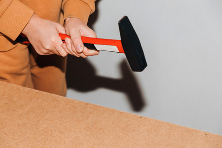 Close-up of boys hands with a hammer driving nails on the back wall of furniture. Front view, selective focusの写真素材