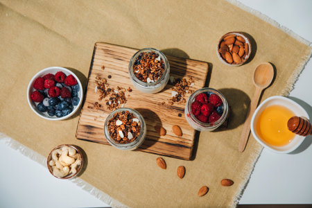 Yoghurts in glass jars with blueberries, raspberries and chia seeds and granola on a wooden board on a white background with tablecloth. The concept of healthy eating. Flat layの写真素材