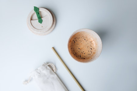 Coffee with foam in an eco glass on a white table with a bamboo straw and an eco bag. Flat layの写真素材