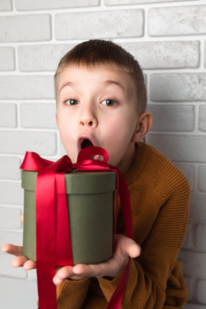 Surprised boy in a yellow sweater holds a green round gift with a red ribbon. Front viewの写真素材