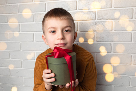 Beautiful boy in a yellow sweater holds a green round gift with a red ribbon. Front viewの写真素材