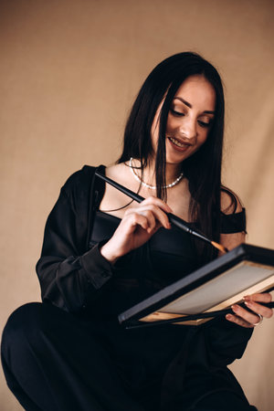 Girl painter in black clothes with a brush sittings on a chair. Portrait of a girl, front viewの写真素材