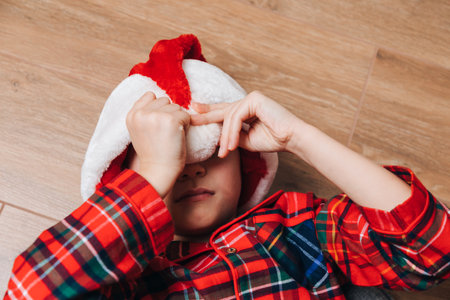 A sleeping boy in red-green pajamas and a Santa hat lies on the floor and close eyes. Christmas at home. Top viewの写真素材