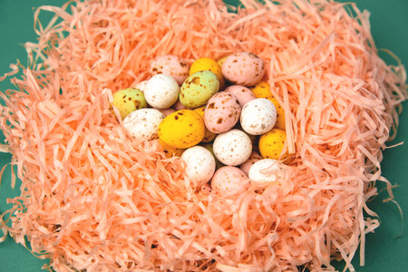 Chocolate colorful decorative eggs on the orange shredded paper on green background. Happy Easter....