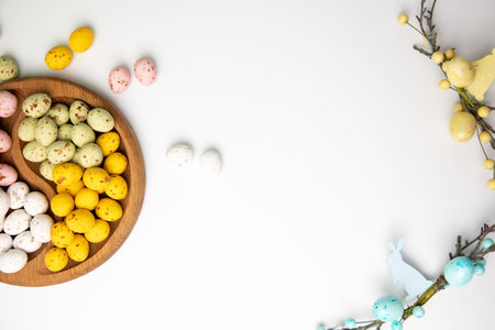 Multi-colored chocolate decorative eggs in wooden plate on a white background with decorative branches. Happy Easter background. Top viewの写真素材