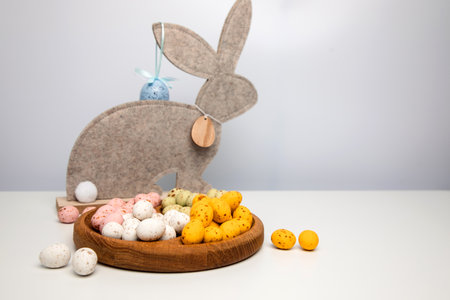 Multi-colored chocolate decorative eggs in wooden plate and gray rabbit on a white background. Happy...