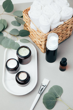 Amber bottles with facial cosmetics and white towels on a tray with a branch of eucalyptus on the gray concrete background. Top viewの写真素材