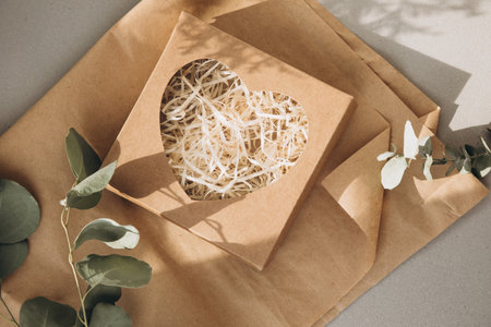 Eco gift wrapping. Cardboard brown gift box with a transparent heart and cut paper inside on sheets...