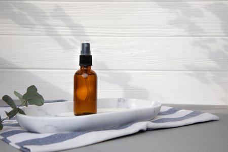 Amber bottle with facial cosmetics on a tray with a branch of eucalyptus on the gray wooden background, facial serum. Front viewの写真素材