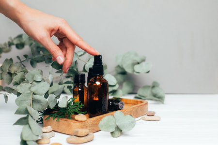 Female hand pushes on amber spray bottle with facial cosmetics on a tray with a branch of eucalyptus on the gray wooden table, facial cleaner, serum. Front viewの写真素材