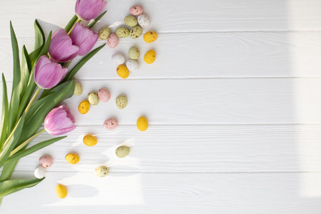 Chocolate colorful decorative eggs and pink tulips on a white wooden table on grey background. Happy...